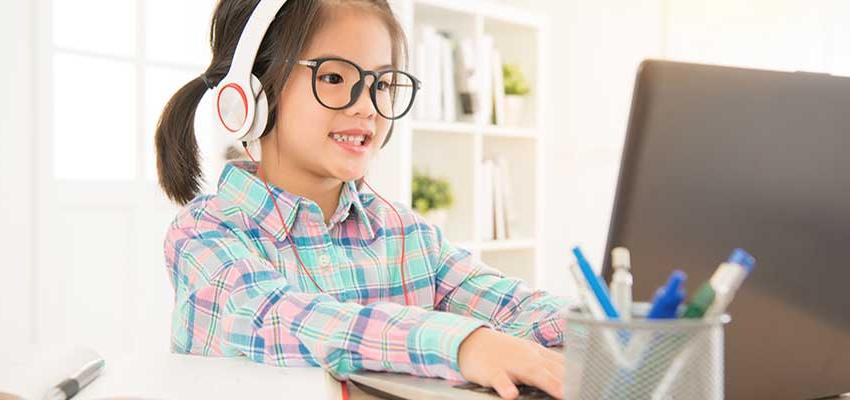 Little girl with headphones on typing on laptop.